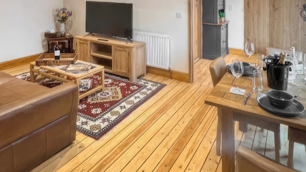 Una sala de estar acogedora con suelo de madera, un televisor sobre un mueble de madera, un sofá, una mesa de centro y una zona de comedor con una mesa y sillas.