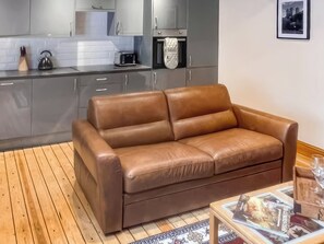 A brown leather sofa in a modern kitchen with grey cabinets, a wooden floor, and a framed picture on the wall. - Stewards Bothy - UK48303 (Berwick-upon-Tweed)