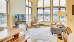 A spacious living room with a large TV, comfortable seating, and large windows offering a city view. - Custom Harborside Loft In the Heart of Ketchikan (Ketchikan)