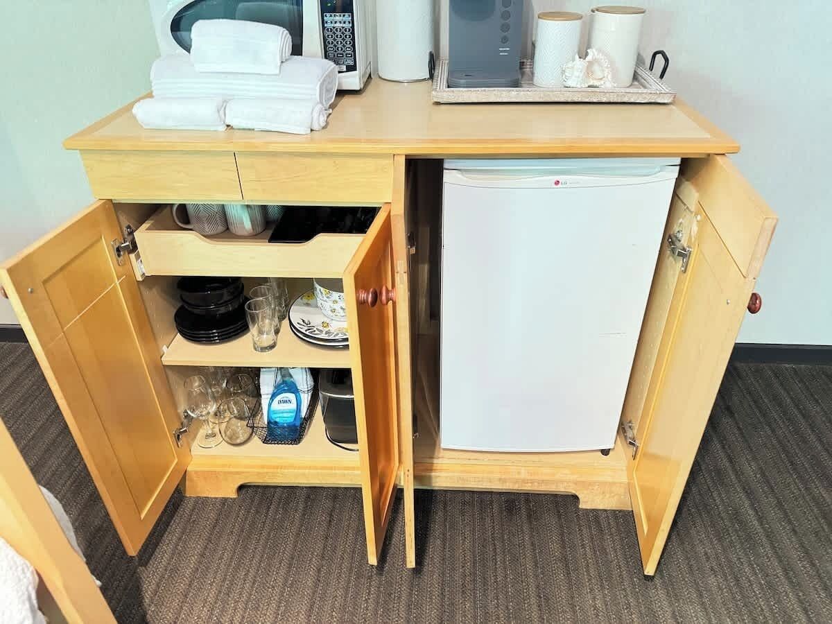 A compact kitchenette with a microwave, a small refrigerator, and a drawer with dishes and glasses.
