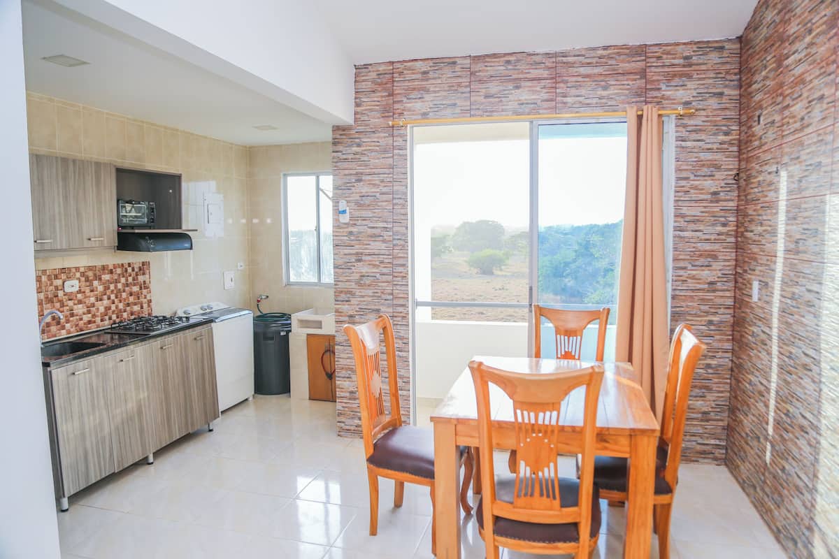 A modern kitchen with a gas stove, a built-in oven, and a microwave. There is a dining area with a table and chairs. The room has a large window with a view of the outdoors.