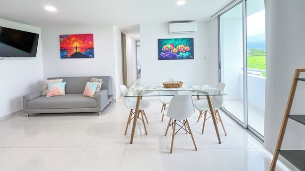 Un salon moderne avec un canapé gris, une table à manger en verre entourée de chaises et des œuvres d’art accrochées aux murs.