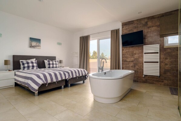 A modern bedroom with a large bed, a bathtub, and a TV mounted on the wall.