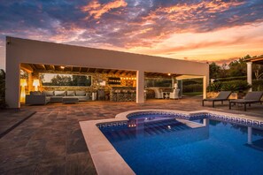 Ein moderner Poolbereich im Freien mit einer terrasse aus Steinplatten, einer integrierten Bar und einer Sitzecke mit einer Couch und Sesseln.