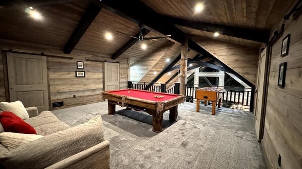 Ein gemütliches Zimmer mit Billardtisch, einer Couch und einer Treppe zu einer oberen Etage.