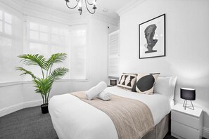 A modern bedroom with a large bed, a potted plant, a framed artwork, and a bedside lamp. - Luxury Apartment - Parking - High-Speed WiFi - Wolverhampton (Wolverhampton)