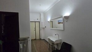 A hallway with a white radiator, a white desk, and a black chair. There is a door at the end of the hallway. - Optima mansio (Roma)