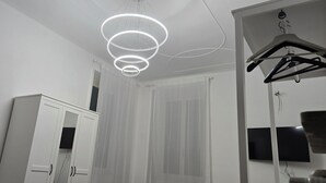 A room with a modern chandelier, a wardrobe, and a television mounted on the wall. - Optima mansio (Roma)