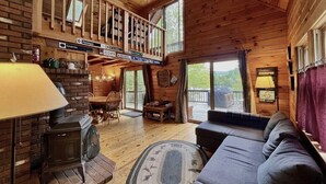 A cozy cabin interior with a fireplace, a sofa, a dining area, and a balcony with a view.