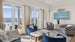 A spacious living room with a view of the ocean, featuring blue and patterned furniture, a wooden coffee table, and a ceiling fan.