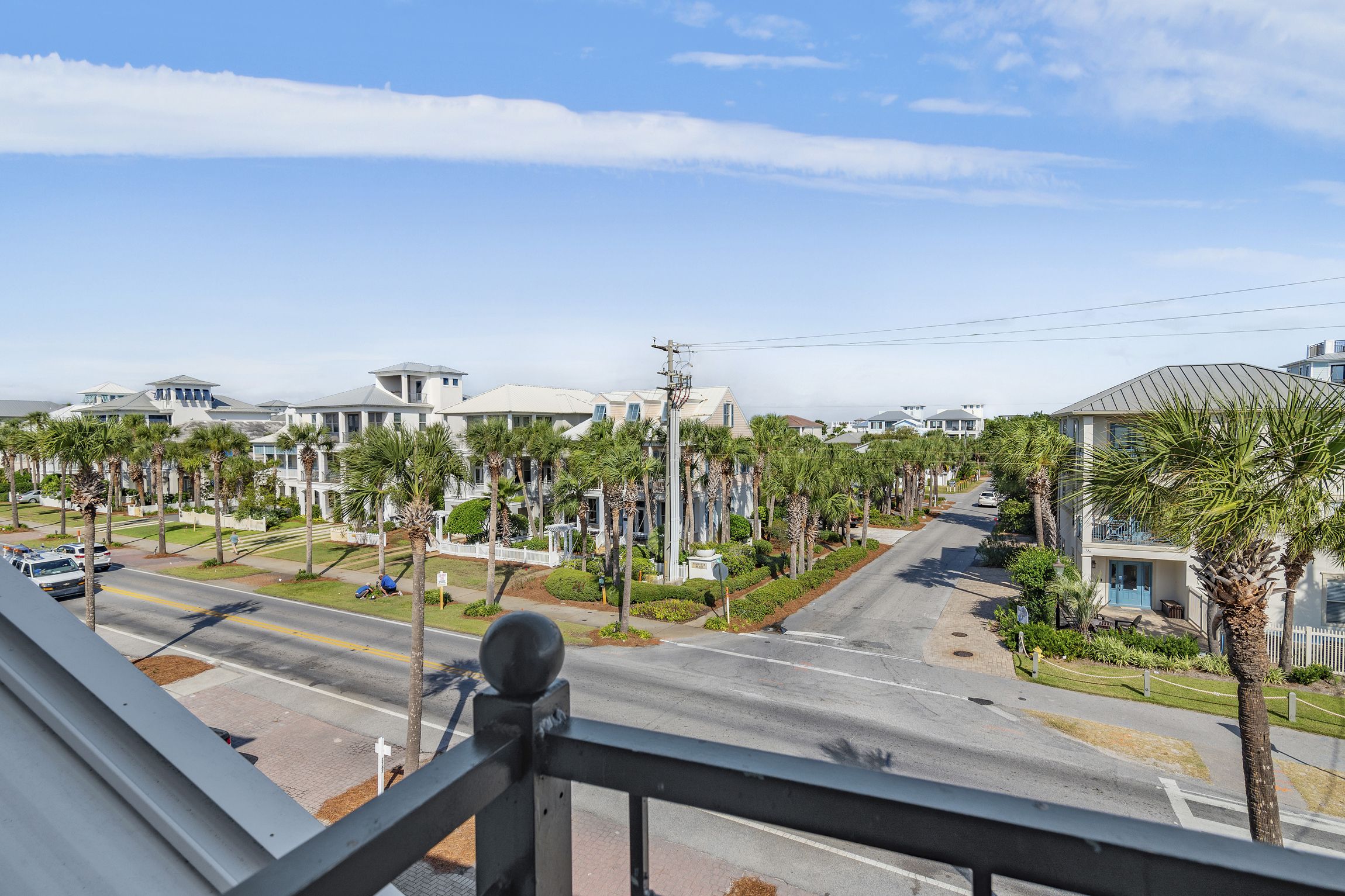 A residential street with houses, palm trees, and a clear sky.