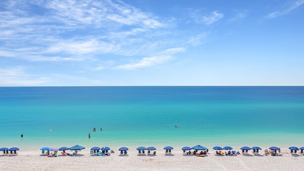 A beach with clear turquoise water, a sandy shore, and several blue umbrellas.