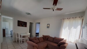 Un saló amb un sofà seccional marró, una taula de menjador amb caires, un ventilador de sostre i una cuina al fons.