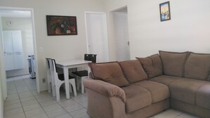 Un saló amb un sofà marró, una taula blanca i cadires. Hi ha un quadre a la paret i una porta que dóna a una altra habitació.