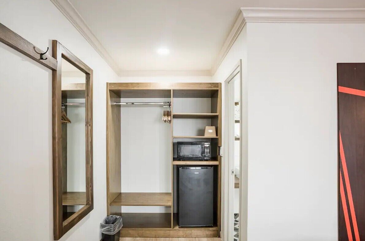 A compact kitchen with a microwave, refrigerator, and wooden shelves.