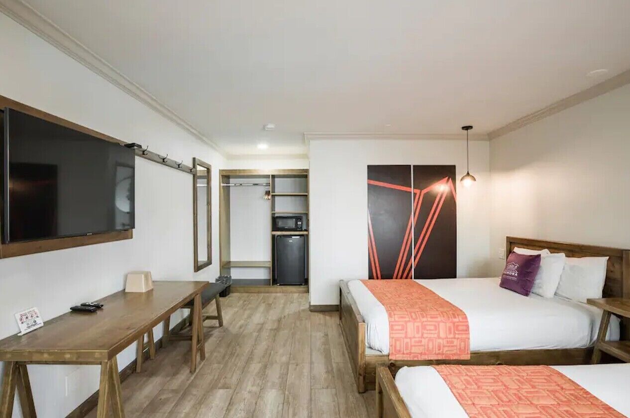 Hotellihuone, jossa on sänky, työpöytä, televisio ja pieni keittiönurkkaus.