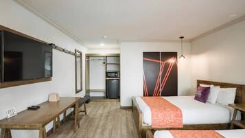 Hotellihuone, jossa on sänky, työpöytä, televisio ja pieni keittiönurkkaus.