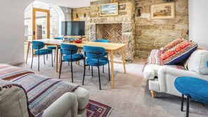 Ein gemütliches Wohnzimmer mit Kamin aus Stein, einem Essbereich mit blauen Stühlen und einem Fernseher auf einem Holztisch.