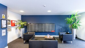 A reception area with a blue wall, a bulletin board, two potted plants, and a seating area with a small table. - Corner House in Sheffield (Sheffield)