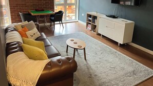 A living room with a brown leather sofa, a small round table, a white cabinet, and a flat-screen TV mounted on a dark wall. - Corner House in Sheffield (Sheffield)