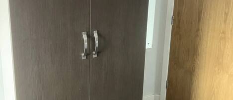 Un armario de madera oscura con dos puertas y tiradores plateados, situado junto a una puerta de madera en una habitación con suelo de madera.