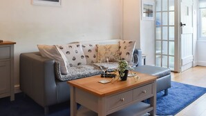Un salon avec un canapé gris, une table basse en bois et une porte en verre donnant sur l’extérieur.