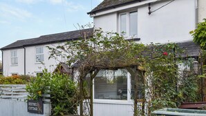 Une petite maison blanche avec une pergola en bois et une enseigne indiquant « Kestrel Cottage ».