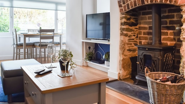 Un salon moderne avec une cheminée en pierre, un coin repas baigné de lumière naturelle et un téléviseur posé sur une étagère.