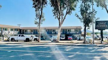 Un motel composé d’un bâtiment à deux étages, d’un parking où sont garées plusieurs voitures et d’un panneau indicateur.