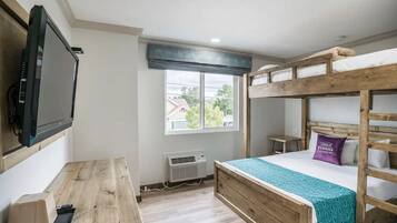 Une chambre avec un lit superposé, une télévision, un bureau et une fenêtre donnant sur des maisons.