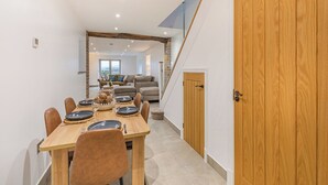 Een eetgedeelte met een houten tafel, stoelen en uitzicht op een woonkamer met een bank en een trap.