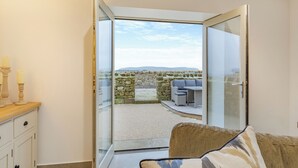 Een kamer met een glazen deur die uitkomt op een terras met stenen muren en uitzicht op het landschap.