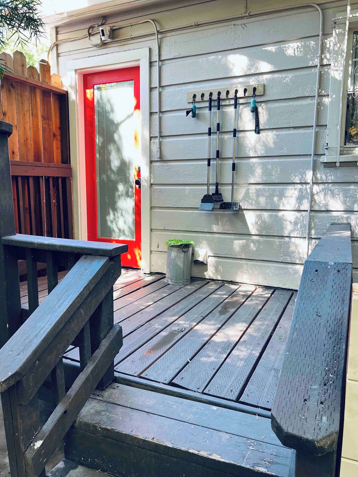A wooden deck with a red door, a trash can, and a wall-mounted broom rack.