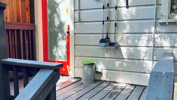 A wooden deck with a red door, a trash can, and a wall-mounted broom rack.