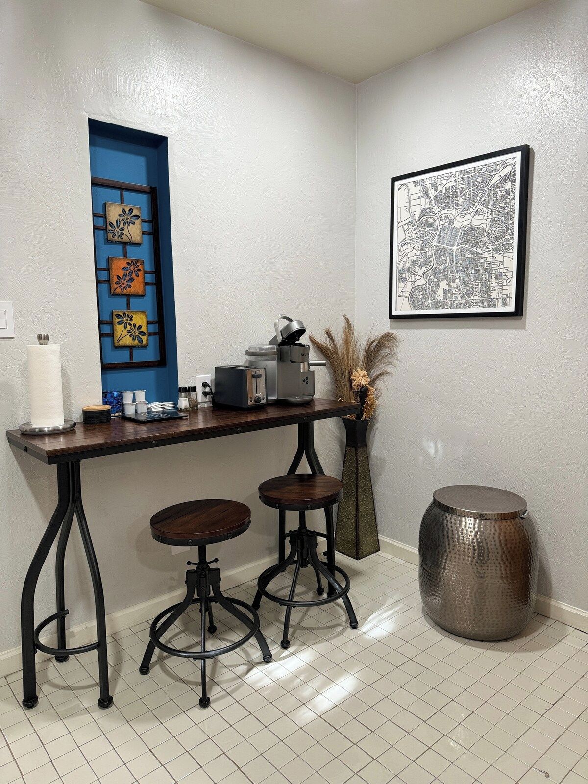 A kitchen area with a bar stool, a coffee machine, and a decorative vase.