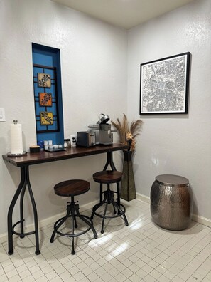 A kitchen area with a bar stool, a coffee machine, and a decorative vase.