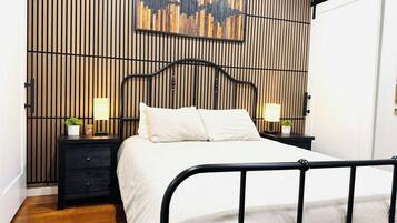 Een slaapkamer met een bed, nachtkastjes, een kunstwerk aan de muur en een zwart metalen hoofdeinde.