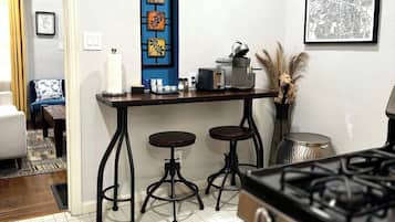 A kitchen with a gas stove, two stools, a coffee machine, and a blue-framed window.