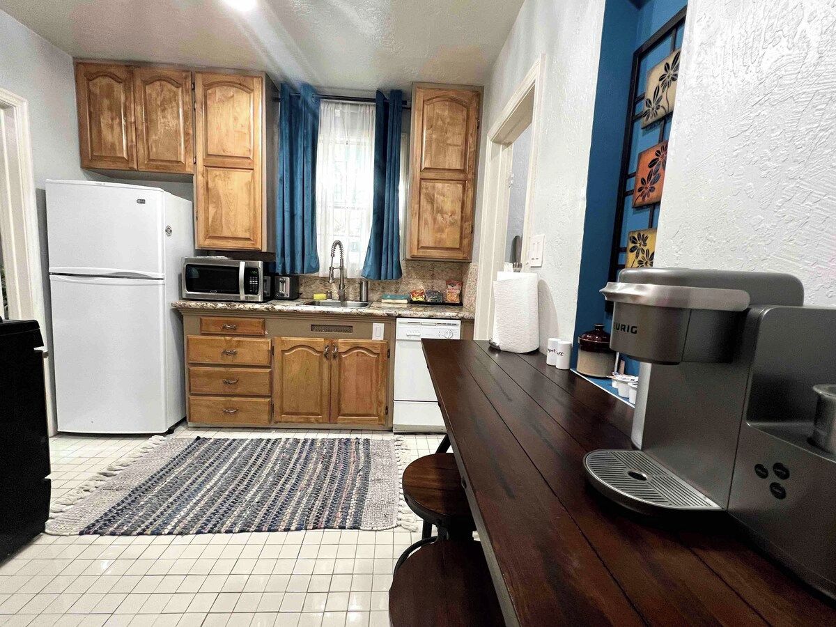 A kitchen with wooden cabinets, a refrigerator, a microwave, a coffee maker, and a tiled floor.