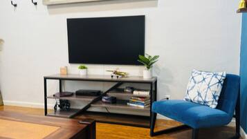 A modern living room with a flat-screen TV mounted on the wall, a blue sofa with a geometric-patterned pillow, a wooden coffee table, and a small plant on a side table.
