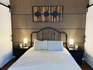 A bed with a headboard, two bedside tables with lamps, and a wall with vertical wooden slats and a decorative piece above the bed. - Classic Midtown 1-Bedroom: Walk to Ice Blocks (Sacramento)