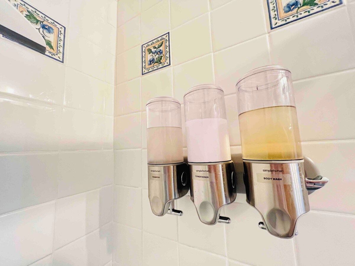 Une salle de bain équipée de trois distributeurs pour le savon, le shampoing et le gel douche.