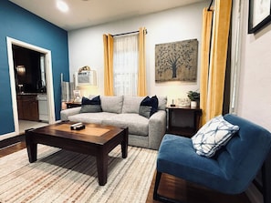A living room with a sofa, a blue armchair, a coffee table, and a small side table with a plant.