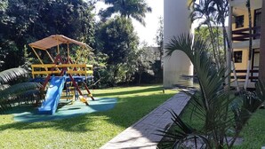 Un'area giochi con scivolo e strutture per arrampicata, circondata da un prato curato e palme.