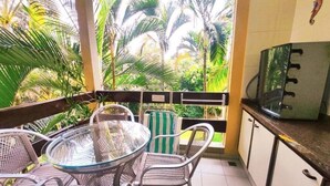 Un balcone con un tavolo e sedie in vetro, una TV e vista su piante tropicali.