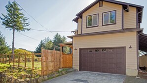 A two-story house with a garage, a wooden fence, and a stone wall. -  Overlooking the ocean, sleeps 7, kid and pet friendly, pergola with privacy. (Whitethorn)