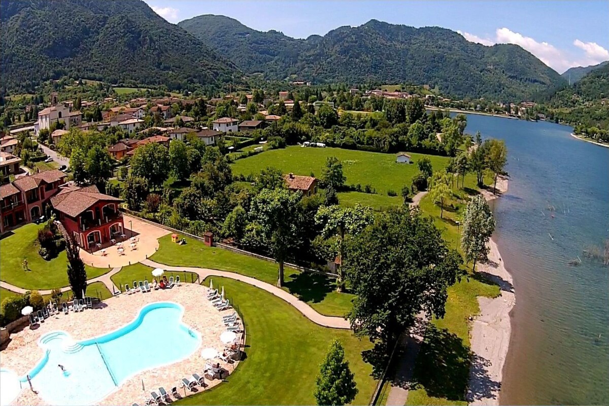 A resort with a swimming pool, lounge chairs, and a view of a lake and mountains.