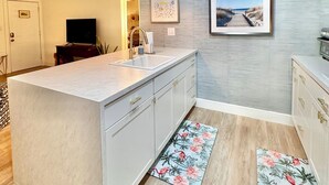 Una cocina moderna con una isla central, una lámpara colgante, un cuadro en la pared y suelo de madera.