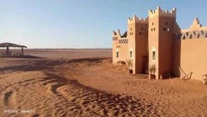 Wüstenlandschaft mit einem traditionellen Lehmziegelgebäude, das zwei Türme und ein kleines Fenster aufweist.