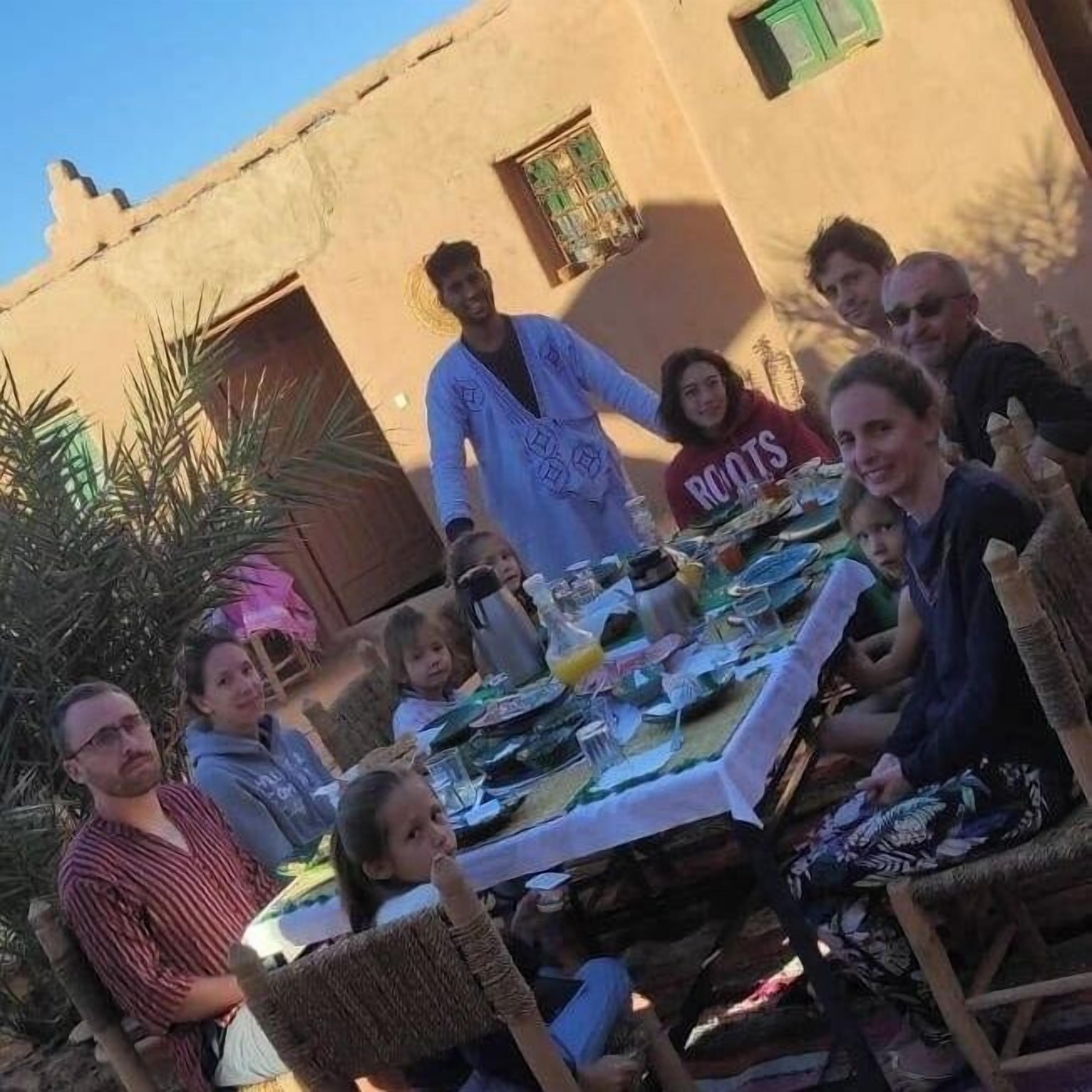 A group of people seated around a table outdoors with a building in the background.
